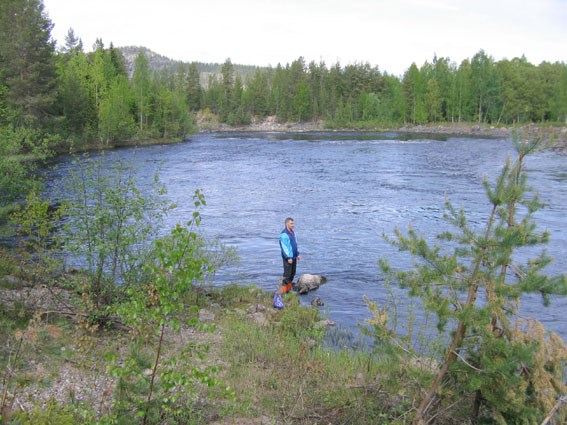 Man som står vid stranden av en älv. Foto.