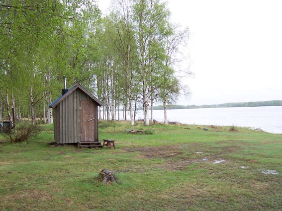 Litet hus framför en bred älv. Foto.