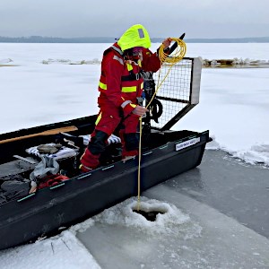 Man standing in a hydrocotper and taking samples from a drilled hole in the ice. Photo.