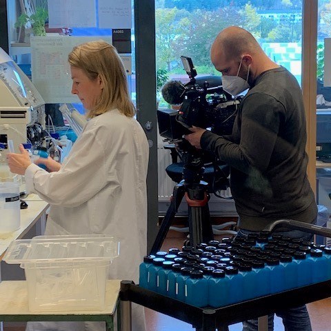 Man som filmar en kvinna som jobbar i ett laboratorium. Foto.