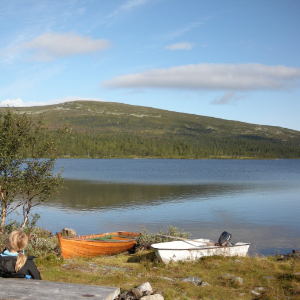 Sjö med fjäll i bakgrunden och två roddbåtar i förgrunden. Foto.