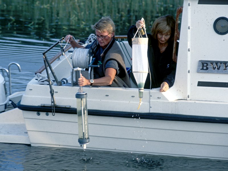 Two persons collecting samples from a boat, photo.