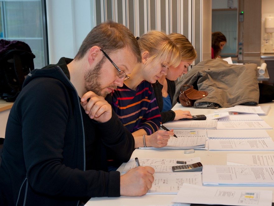 Student writing on papers in a lecture room, photo.