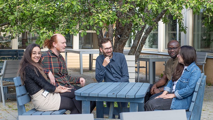 Five people sitting around a table under an apple tree.