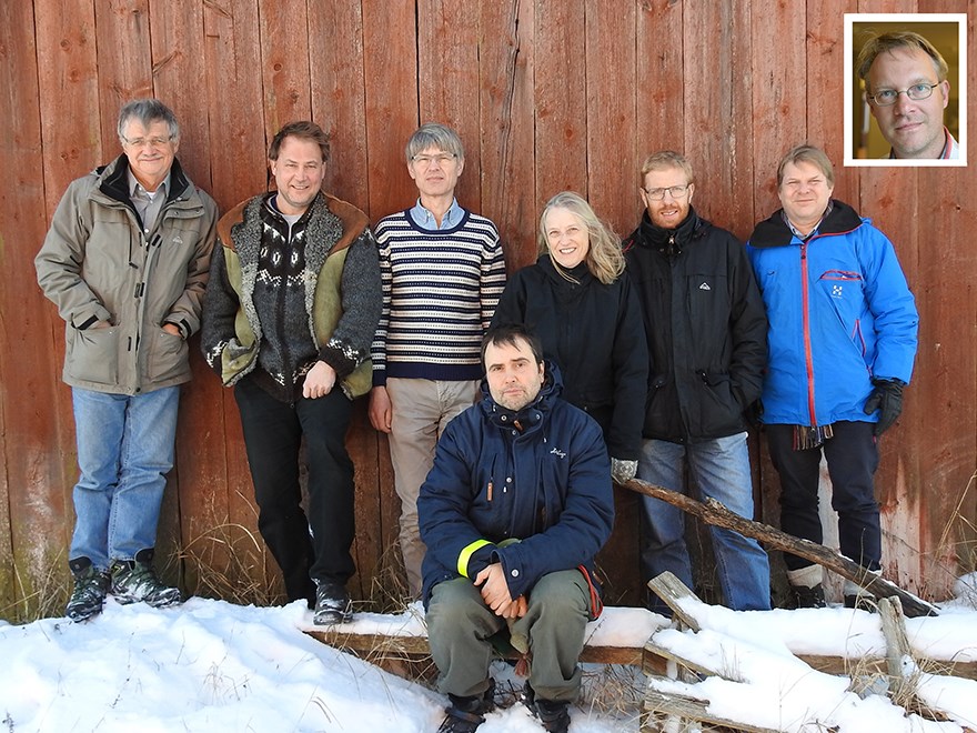 Personer som står mot en röd husvägg, en person sittandes framför och ett inklippt foto.