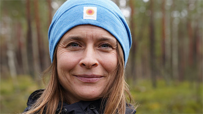 Brun-blond kvinna med blå Stora Enso-mössa i skog. Foto