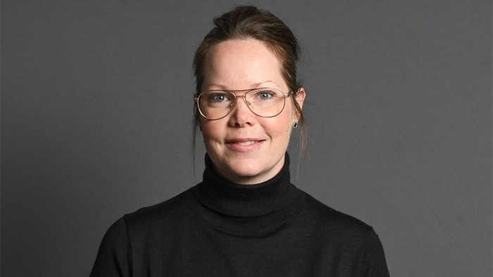 Mörkhårig kvinna med uppsatt hår och svart polotröja. Foto