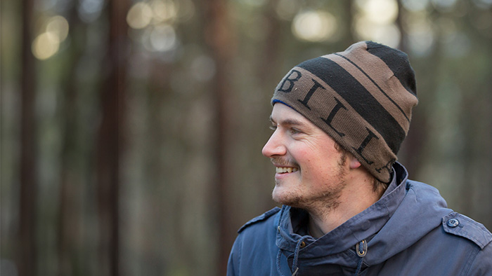 Leende man i mössa och jacka utomhus i profil. Foto