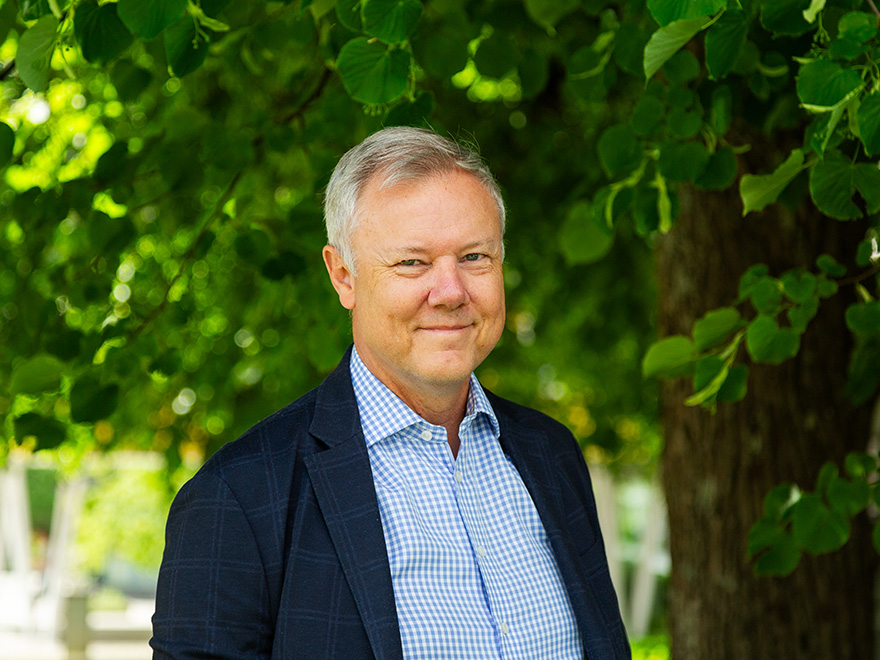 Man med kort grått hår som ler i skjorta och kavaj under ett träd.