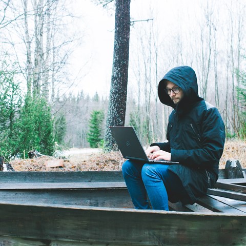 Man med dator i knäet, i en eka i skogen, foto.
