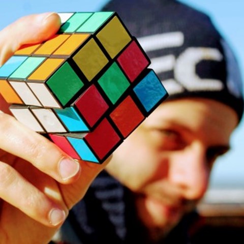 A man holds up a rubics cube, outside. 