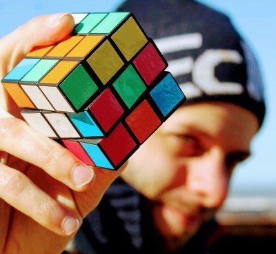 A man holds up a rubics cube, outside. 