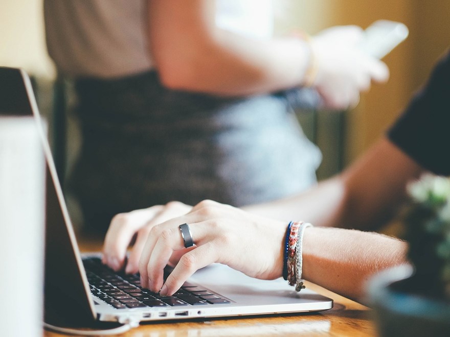 Hands and arm of a person writing on a laptop.