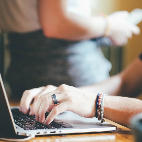 Hands and arm of a person writing on a laptop.