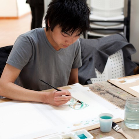 Ung person målar med vattenfärg, sittandes vid ett bord