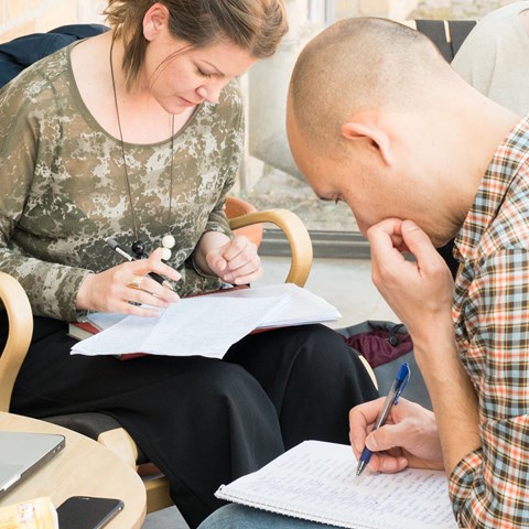 Two students in armchairs, writing in notebooks. 