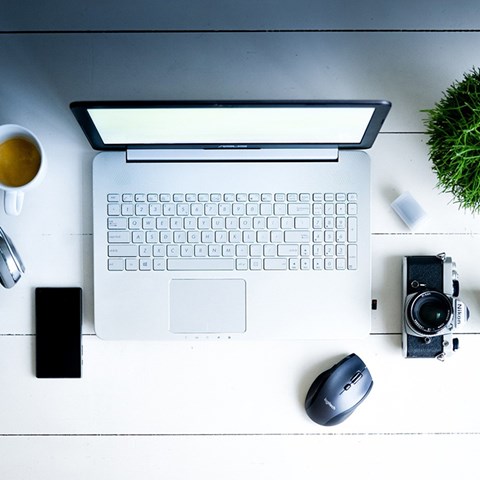 A table with a computer, a cup of coffee, phone, camera and a plant. Photo.