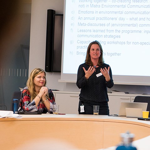 One woman is sitting and one women is standing, having a presentation. Foto.