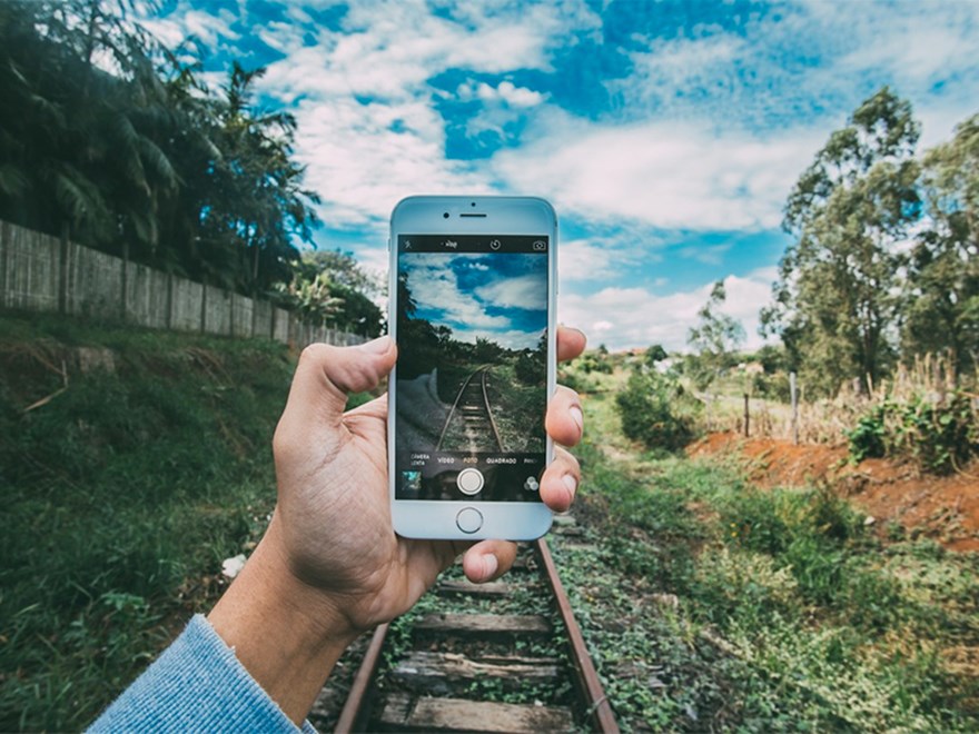 A phone is held in front of train tracks, photo.