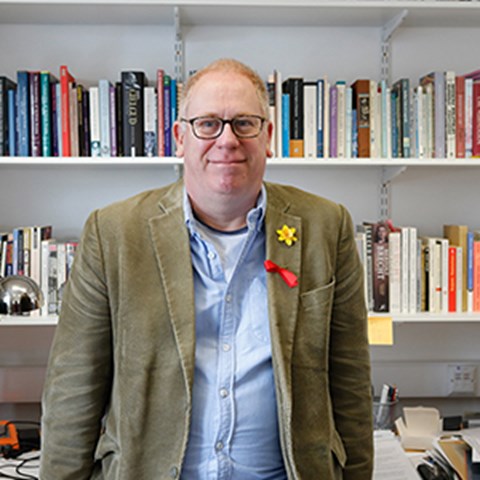 Portrait image of man in front of bookshelf and desk. Photo