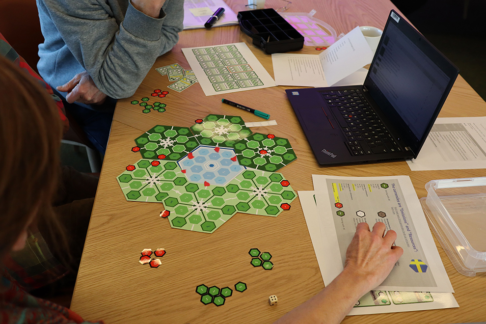 Two people are sitting at a table with a game board and paper in front of them. Photo. 