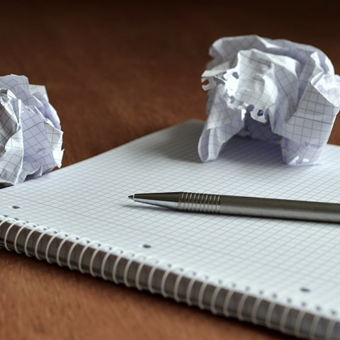 Ett anteckningsblock, två ihopskrynklade pappersark och en penna på ett bord. 