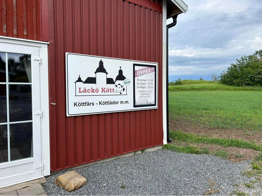 Rött hus med vita knutar, på väggen sitter en skylt med texten "Läckö kött".