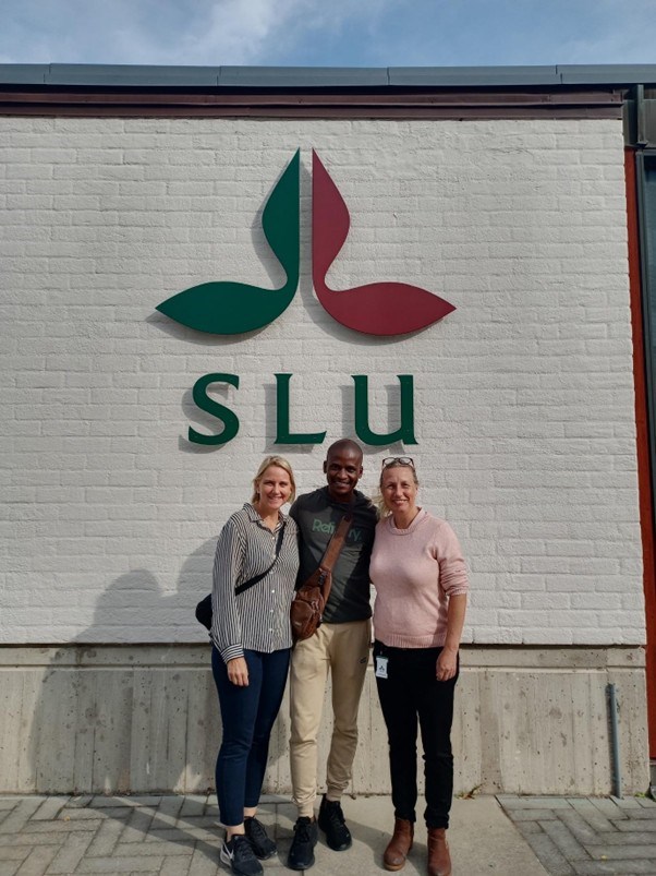 Three people standing in front of a building wall with the SLU logo in the background