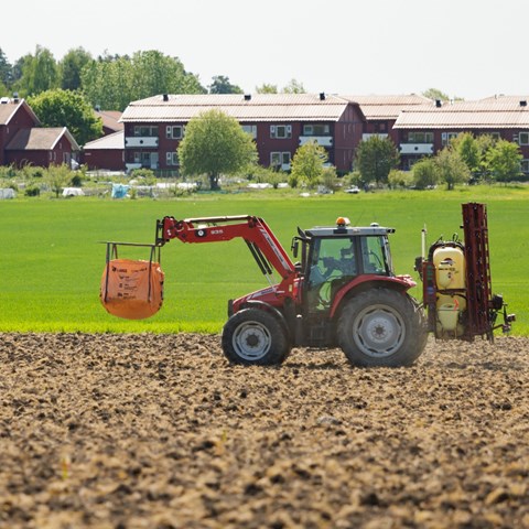 A red tractor transports an orange bag in an arable field
