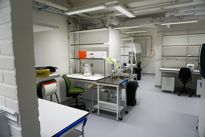 Laboratorium med vita bänkar, diskbänk, hyllor och viss laboratorieutrustning