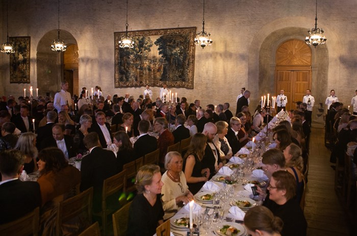 Bilden visar banketten i Uppsala slotts Rikssalen. Långa bord med kandelabrar, sittande gäster i en stor sal.