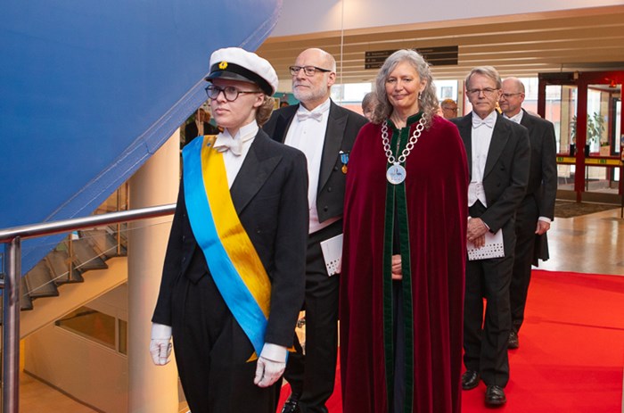 Högtidsklädda människor går i procession. En av dem har stor halskedja och röd sammetskåpa. 