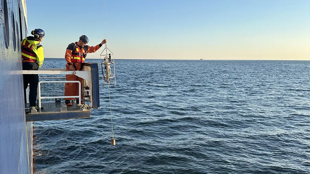 Två personer vinschar upp provtagningsutrustning ur havet