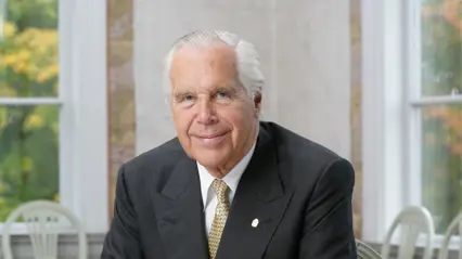 An elderly man in a suit and tie sitting at a table.