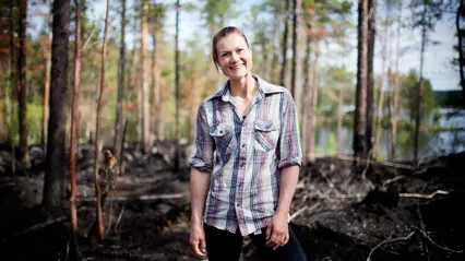A woman standing in the woods with a smile on her face.