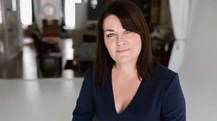 A woman with dark hair, wearing a dark blue shirt posing for an image.