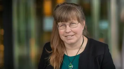 A woman with brown long hair and wearing glasses and a green shirt.
