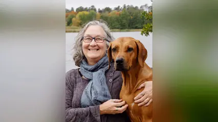 A woman holding a dog in front of a body of water.