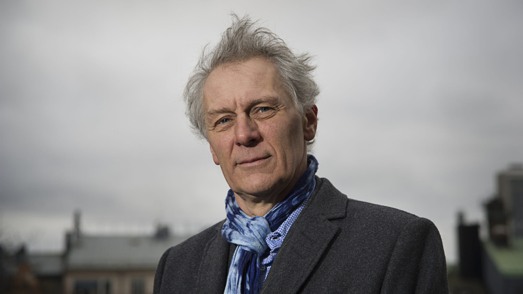 En man med grått hår och blå skjorta.