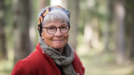 An elderly woman with a scarf, a red jacket and glasses.