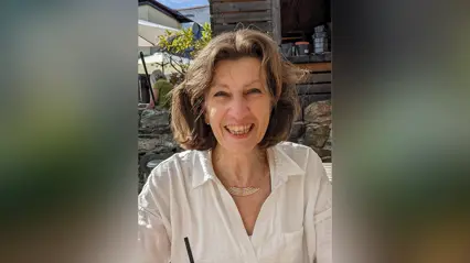 A woman in a white shirt, sitting outside smiling into the camera.