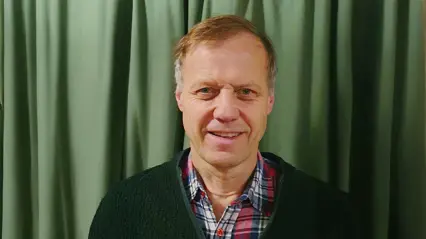 A man standing in front of a green curtain.