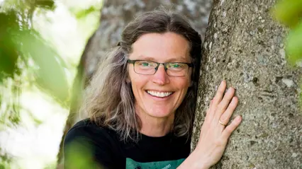 A woman wearing glasses hugging a tree.
