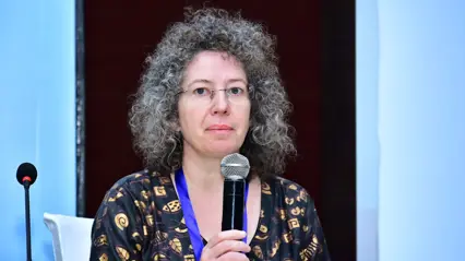 A woman in grey curly hair holds a microphone in front of her.