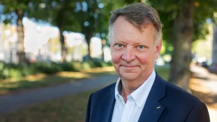 A man in a suit smiles into the cameran.