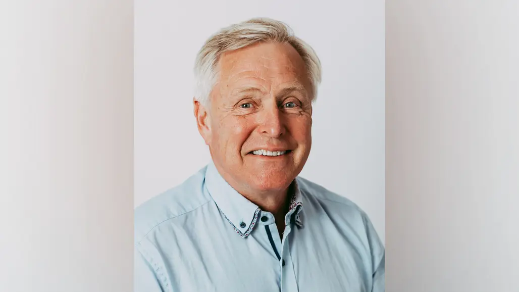 En leende man med grått hår och ljusblå skjorta.