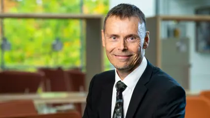 A smiling man in a dark suit looks into the camera.