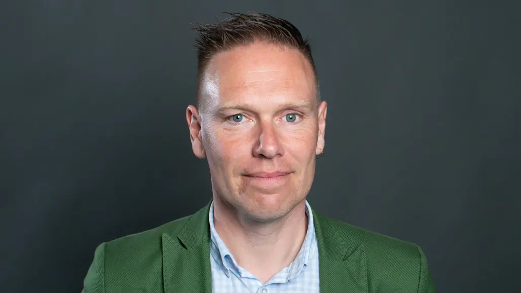 En man klädd i grön jacka och blå skjorta.