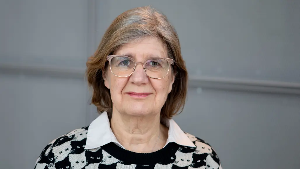 A woman with a bob haircut, glasses and a shirt with a cat pattern looks into the camera.