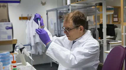 En person står i ett labb och pipetterar.